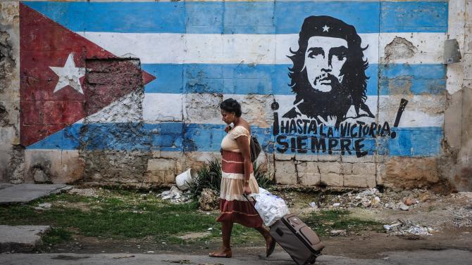 462017810-woman-walks-by-a-mural-with-the-cuban-flag-and-an-image